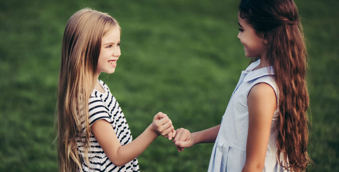 Little pretty girls having fun outdoor. Two cute girls are standing on green grass and holding little fingers. Best friends.