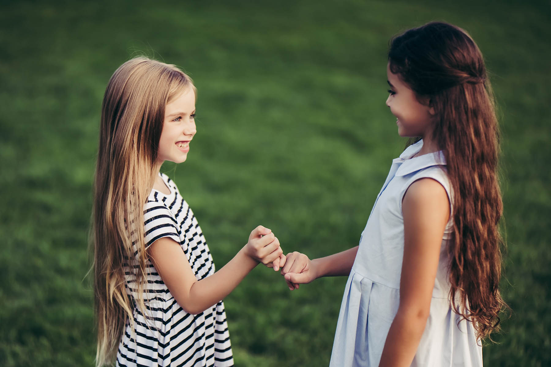 Little pretty girls having fun outdoor. Two cute girls are standing on green grass and holding little fingers. Best friends.