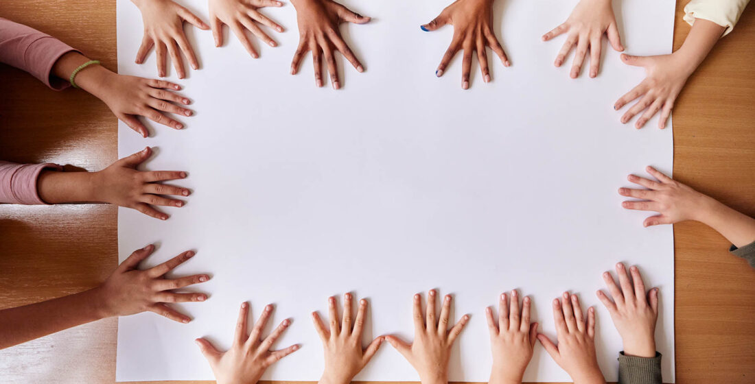 High angle view of large group of unrecognizable children's hand on blank white placard in the classroom. Copy space.